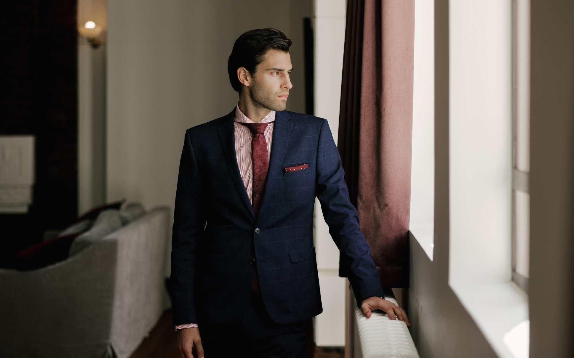 model wearing a red stripe extreme cutaway collar shirt paired with a navy suit and burgundy tie and pocket square